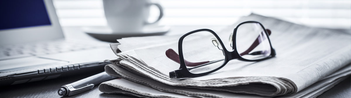 Zeitung, Brille und Notizbuch als Symbol für journalistische Recherche